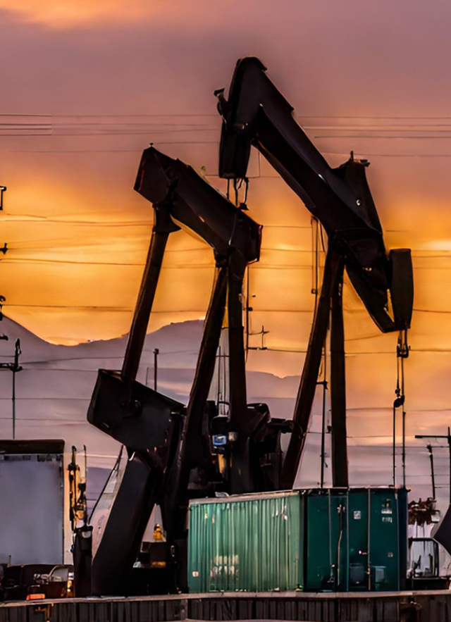 oil rigs with a train and mountains in the background against a purple and orange sunset