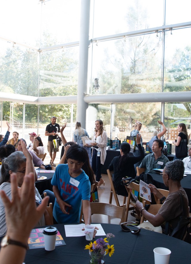 Educators raise their hands as they engage in a presentation led by School Programs staff