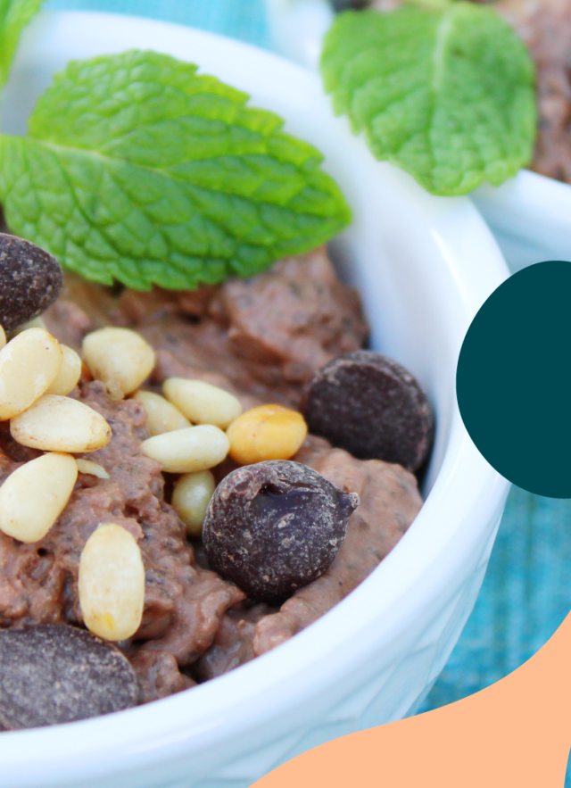 Chocolate chia pudding in a small bowl topped with pine nuts, mint, and chocolate chips