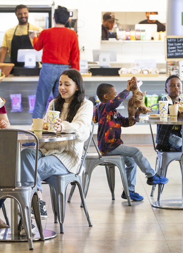 Visitors eating at tables with customers at the counter and snack shelves in the background