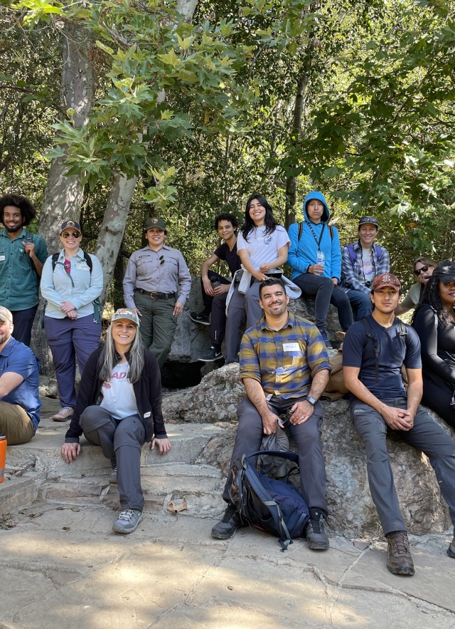 Group of students, NHM employees, and nature guide sitting and standing with trees in the background