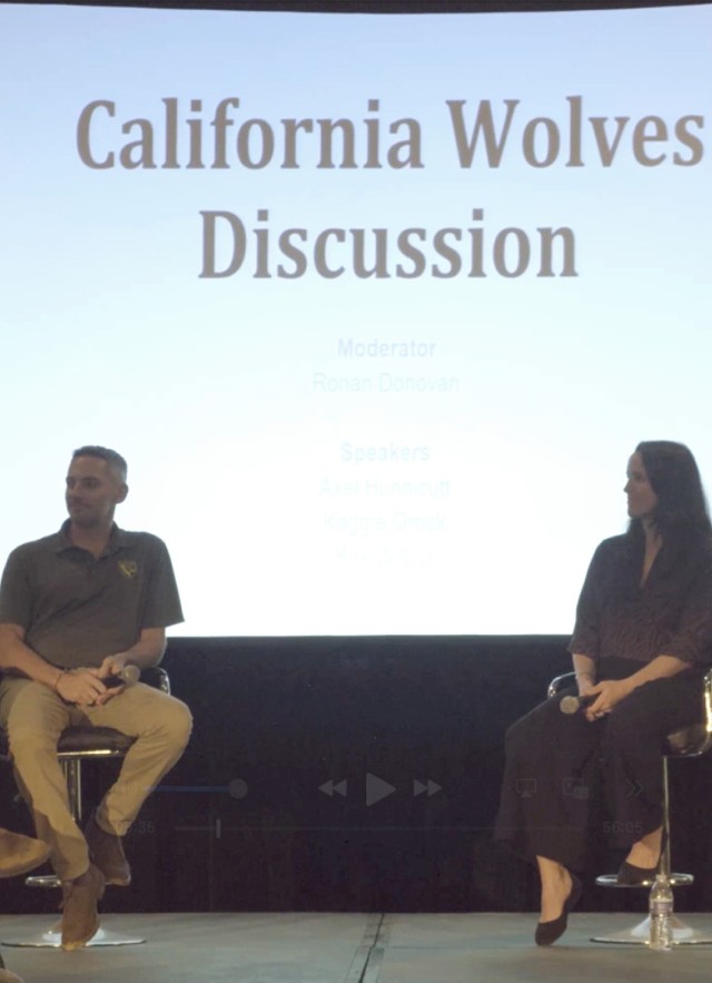 Four people sitting in swivel chairs on a stage with a screen behind them with the title &quot;California Wolves Discussion&quot;