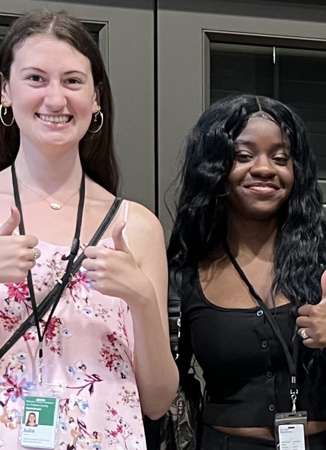 Three interns, wearing ID badges, from the waist up smiling and holding thumbs up