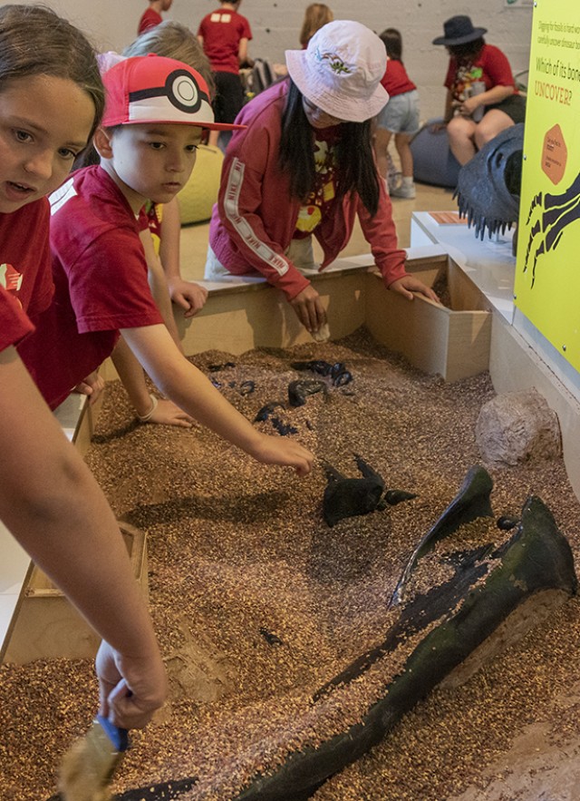 Children digging in a rocky, sand trough with replica fossils