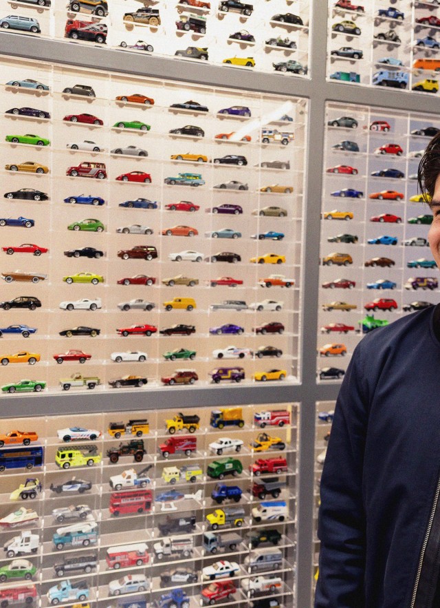 A smiling man stands in front of a display of about 800 Hot Wheel and Matchbox cars