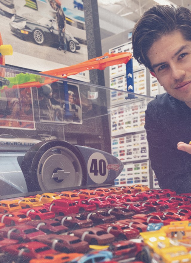A man holds a die cast car over a colorful dislay of more die cast cars
