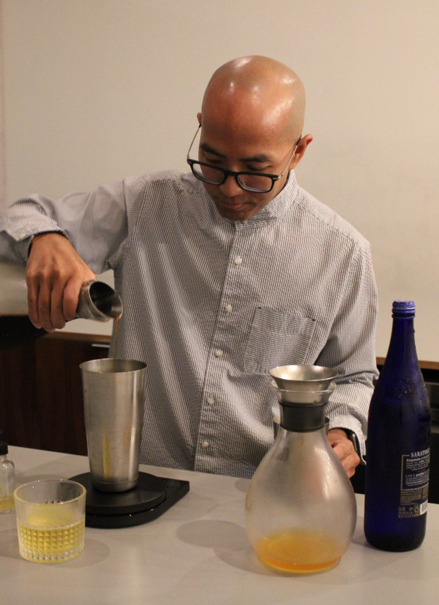 Bald man with black-rimmed glasses behind a minimalist bar, mixing a coffee cocktail.