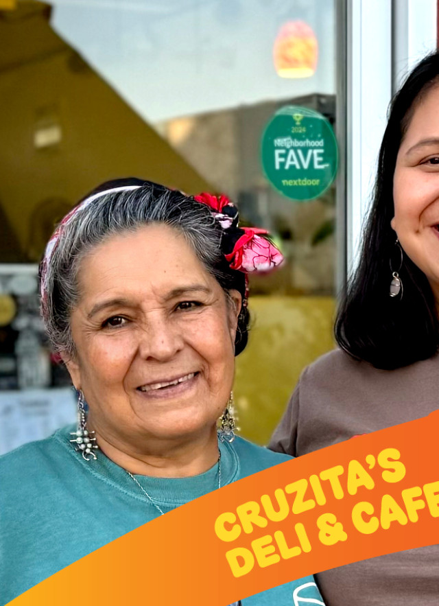 Two women stand together and smile warmly in front of the glass entrance of Cruzita's Deli. A vibrant orange graphic at the bottom includes the business name and a cup of their signature deep red strawberry jamaica.