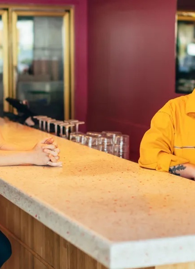 Two women posing on either side of a marble bar, one sitting and one standing.