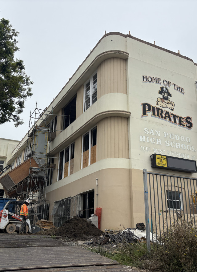 A high school building with the words 'San Pedro Pirates' surrounding an image of a pirate mascot on the building. Signs of construction surround the building 
