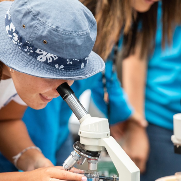 girl with a blue bucket hat looks ithrough a microscope