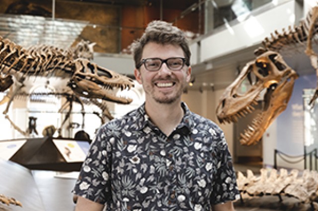 Head and shoulders portrait of Hank Woolley standing in front of two dinosaur skeletons