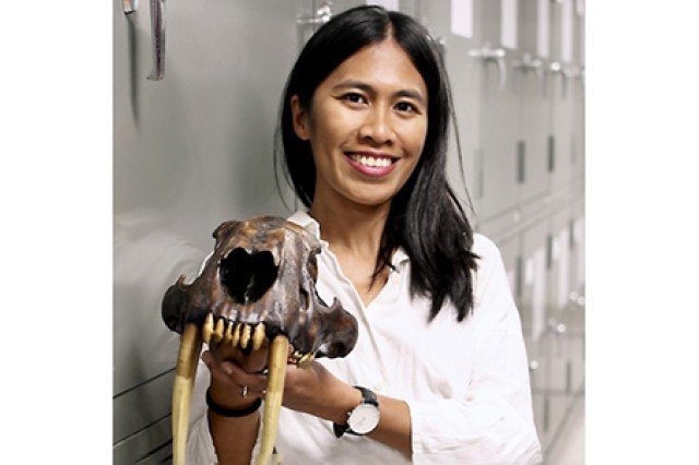 Head and shoulders portrait of Mairin Balisi standing against gray cabinets and holding a saber-toothes skull in her hands