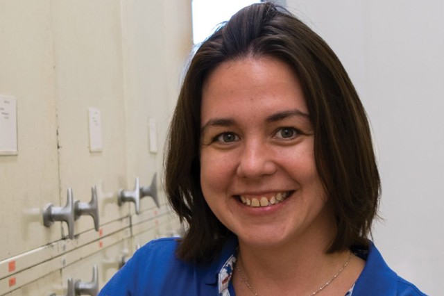 Head and shoulders portrait of Dr. Rachel Racicot wearing a blue shirt with beige specimen cabinets in the background