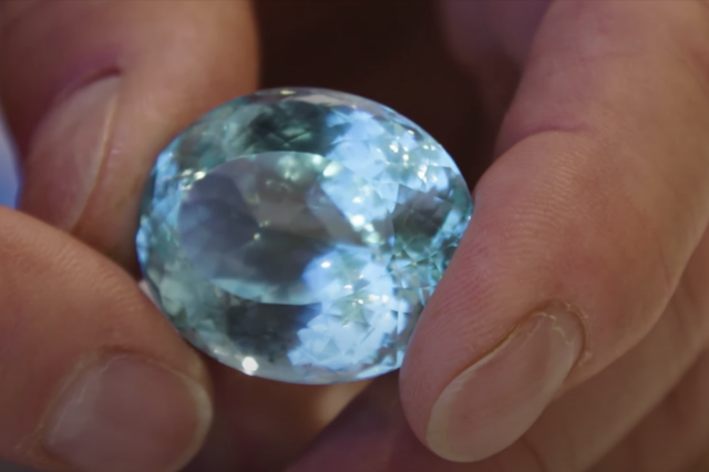 A hand hold an aquamarine colored gemstone