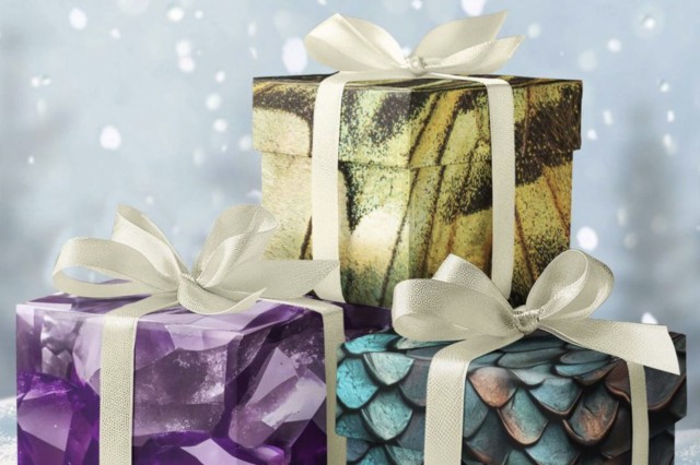 one present on top of two other presents, wrapped in gold, purple, and green scale-shaped wrapping paper with cream bows