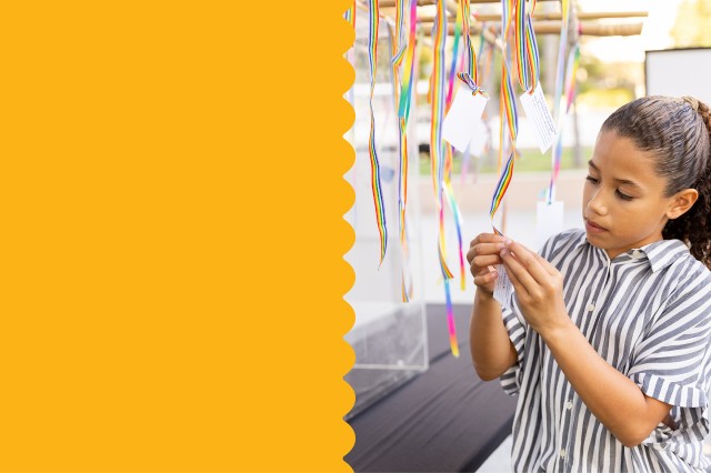 Child in striped shirt looking at a card hanging from a rainbow-striped ribbon