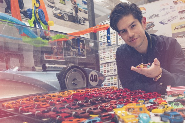 A man holds a die cast car over a colorful dislay of more die cast cars