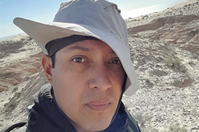 Dr. Adolfo Pacheco Castro wearing a tan flipped up on one side, with a rocky terrain and blue sky in the background