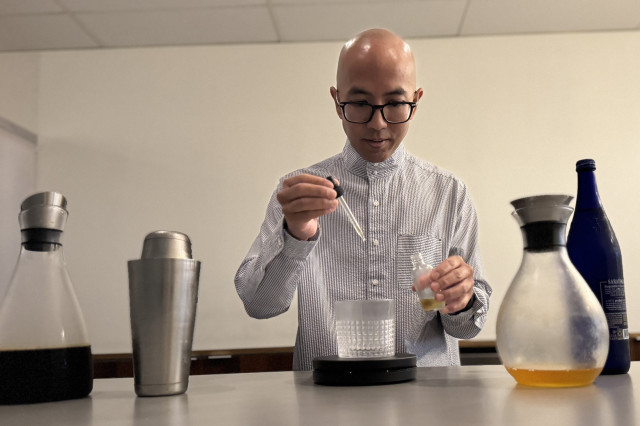 Bald man in glasses using a pipette to measure ingredients into a custom coffee drink.