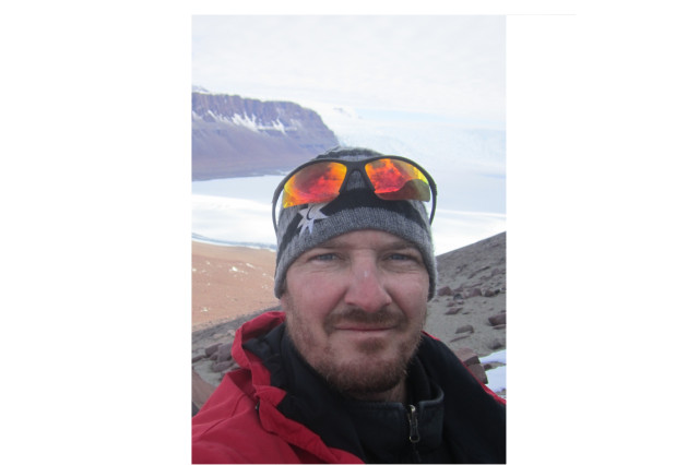 Dr. Nathan Smith wearing goggles on his head with the mountains and ocean behind him