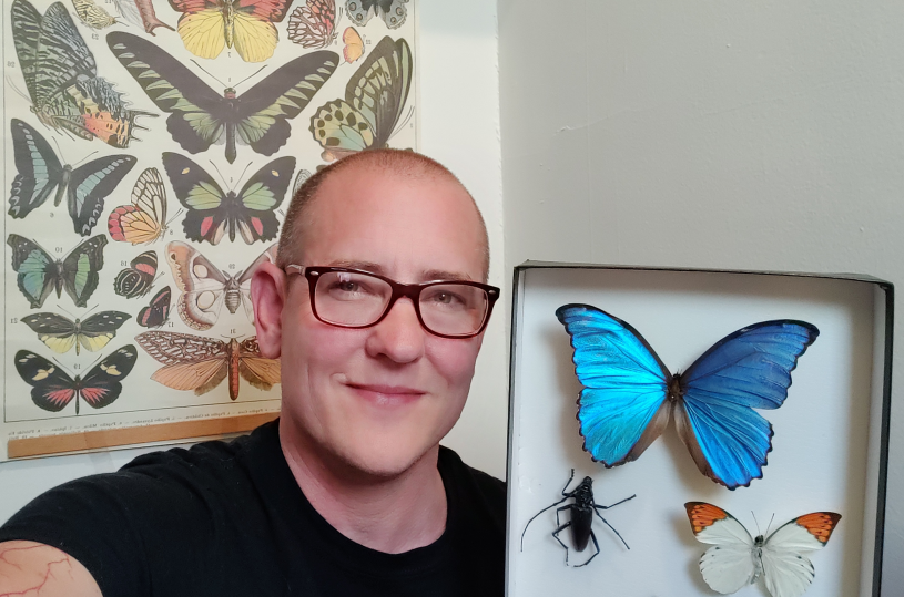 Image of Forest Urban holding a display of pinned butterflies. 