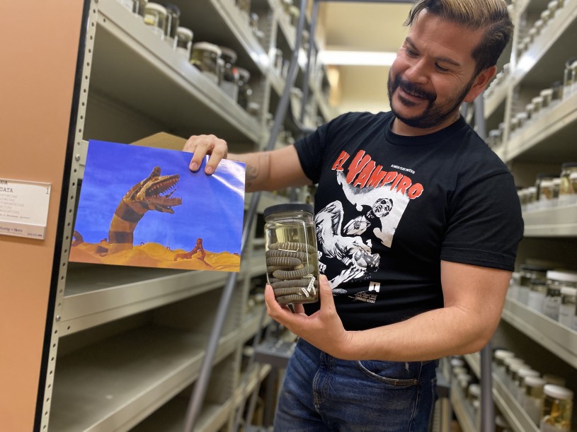Herpetology Collections Manager Neftali Camacho holds a jar of Caecilians next to a sand worm from Beetlejuice