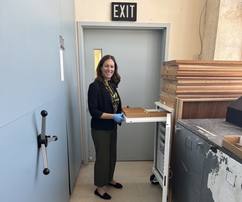 A woman stands in front of an open cabinet beneath an exit sign surrounded by closed shelving
