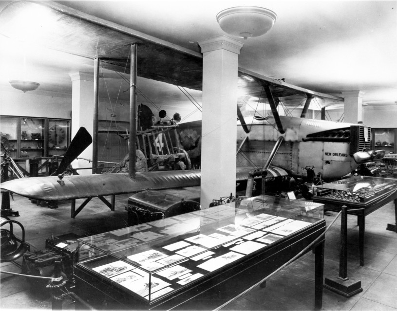 A black and white photograph of a biplane inside a museum exhibition