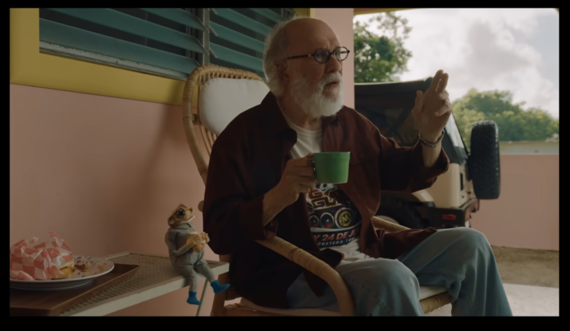 a small frog wearing a speed suit sits next to an old man on a bench