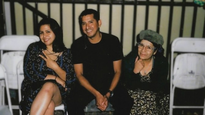  Celina, Jose, and Maricruz sitting and smiling together in front of a dark metal railing.