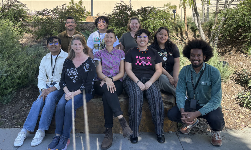 A group of people sit with trees and shrubs in the background