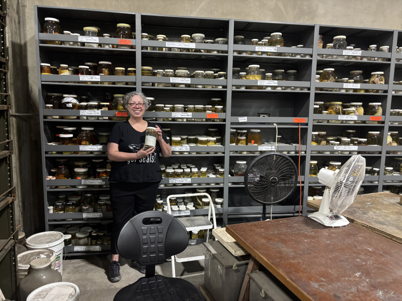 A woman holds a jar in front of a shelf 