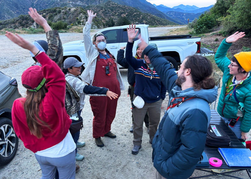 A group of eight people in warm clothes put their hands into a circle