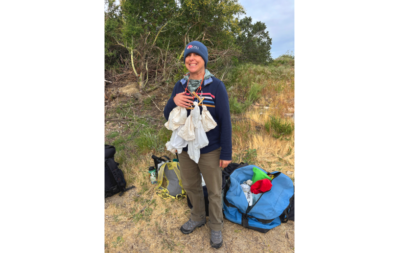 A women in a beanie and jacket smiles with a half-dozen bags strung over her shoulder