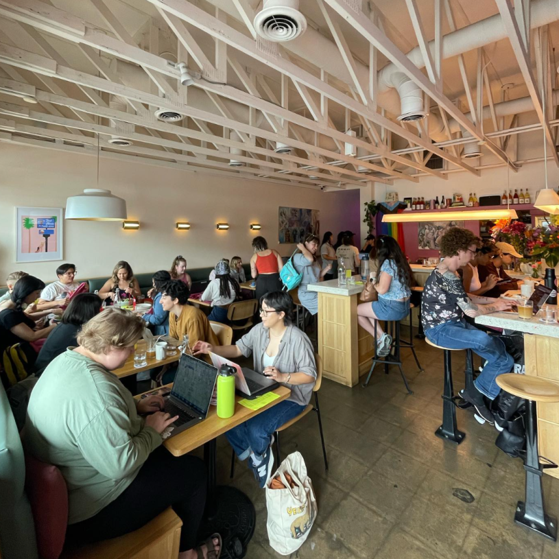 Packed tables at a bar during the day with people working on laptops and having a meal. 