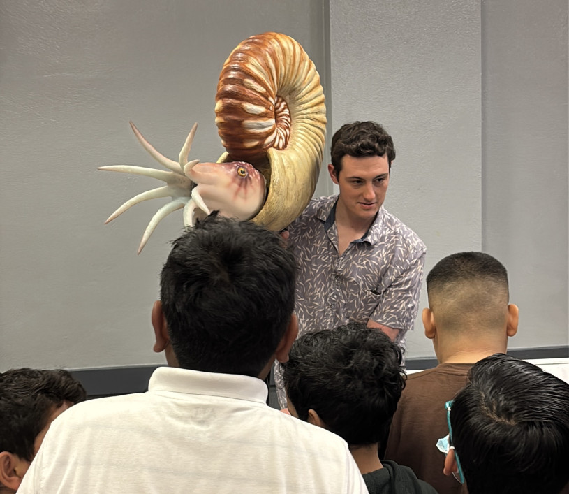 A man holds an ammonite puppet in front of school kids. 