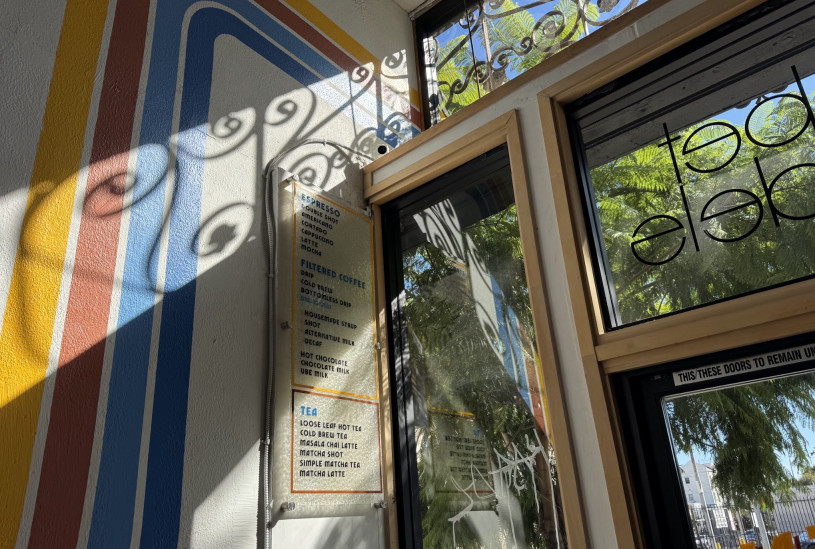 a corner of the coffee shop holds a menu sign painted on the building's original 1920's glass, with the metal work casting an intricate shadow across it and the painted wall. 