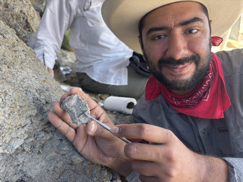 A young bearded man with a red bandana around his neck shows off a vertebrate fossil