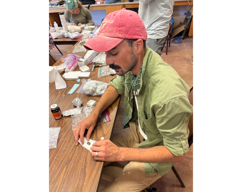 Man in a red hat and green shirt looks at fossil