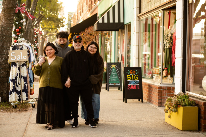 Filipino family with mom, dad, son, and daughter, in a group hug on a sidewalk next to boutique shops.