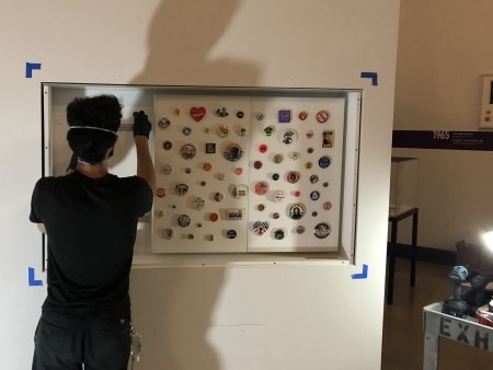 Lead Preparator Eric Sick installing boards with buttons attached into a cutout rectangle in the wall