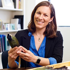 Head and shoulders portrait of Allison Shultz wearing a blue shirt and black blazer and holding a bird specimen