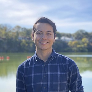 Head and shoulders portrait of David Ledesma wearing a blue plaid shirt with a lake and trees in the background