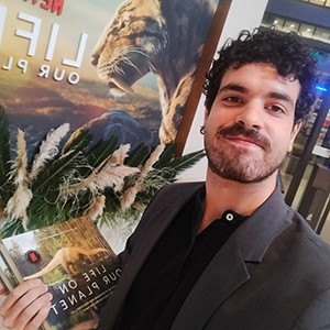 Head and shoulders portrait of Dr. Sergio Martínez Nebreda holding a book in front of a poster of a saber-toothed cat