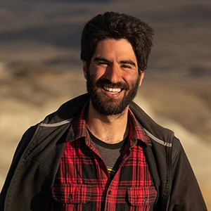 Head and shoulders portrait of Dr. Sebastián Rozadilla wearing a red plaid shirt against a sandy background