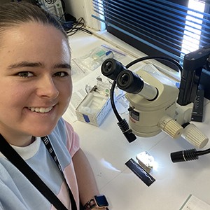 Kristin Watmore wearing a black lanyard and leaning on a table with a microscope