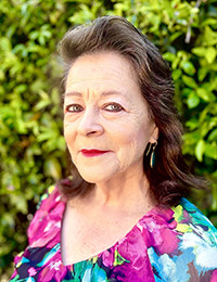 Barbara Carrasco, in a flora blouse, against a green leafy background