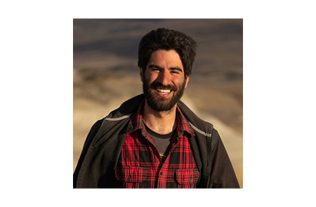 Head and shoulders portrait of Dr. Sebastián Rozadilla wearing a red plaid shirt against a sandy background